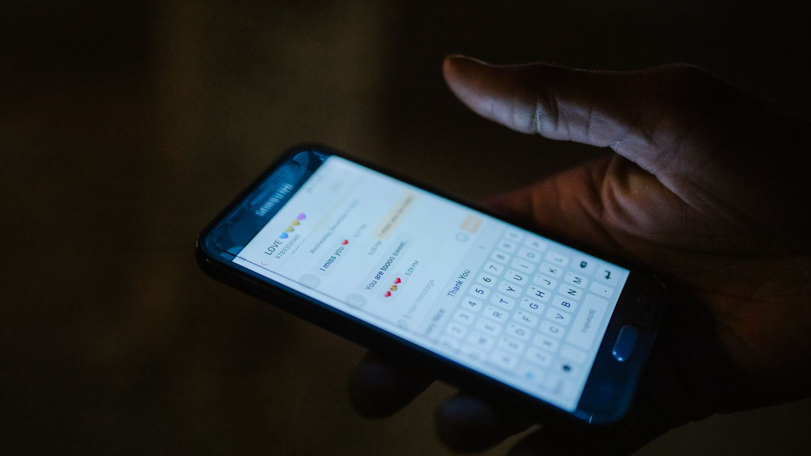 A hand holding a smartphone with a messaging app open in a softly lit café.